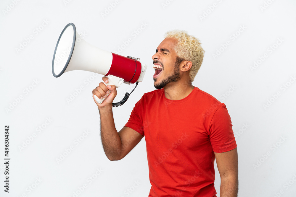 Young Colombian handsome man isolated on white background shouting through a megaphone to announce something in lateral position Young Colombian handsome man isolated on white background shouting through a megaphone to announce something in lateral position