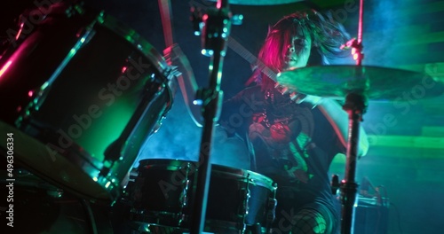 Young beautiful girl playing drums on the stage of nightclub