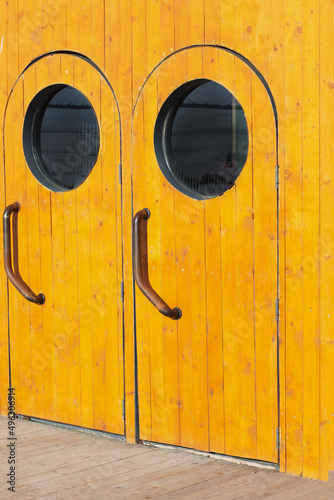 Wooden brown door entrance exit in nautical marine style with a porthole on an old vintage ship boat