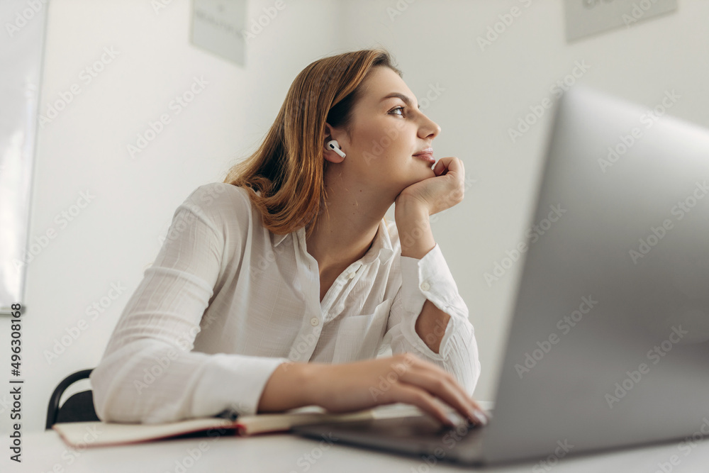 A bored young woman sits at her home office desk, looks at a distance, cannot work at a laptop, an exhausted student feels unmotivated, unwilling to learn, distracted by a break. A bored young woman sits at her home office desk, looks at a distance, cannot work at a laptop, an exhausted student feels unmotivated, unwilling to learn, distracted by a break.
