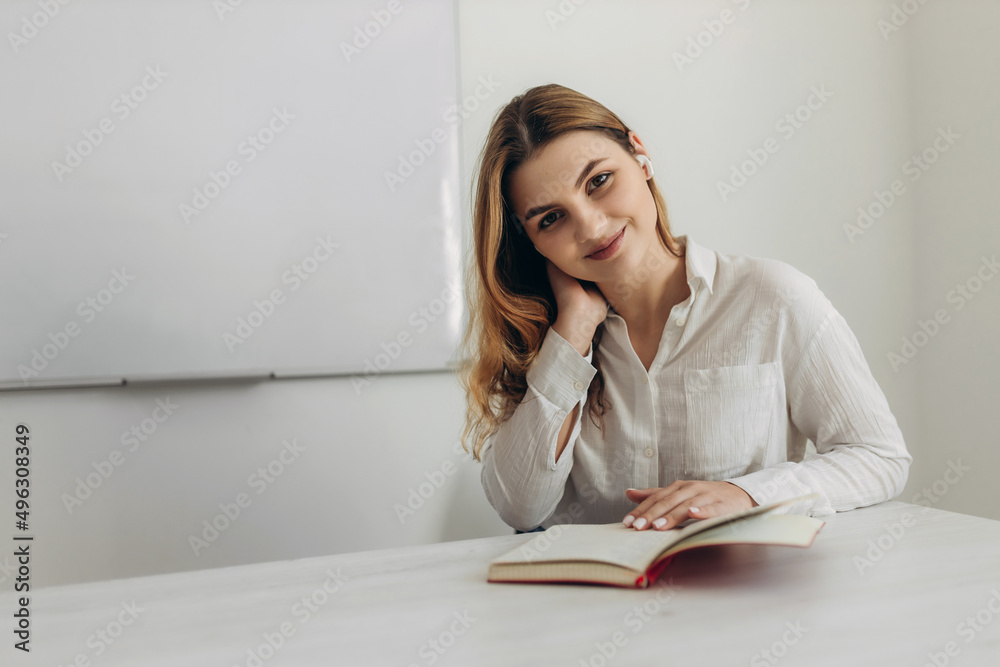 Portrait of a young teacher in the classroom. Girl holding a red notebook. Preparation for distance learning Portrait of a young teacher in the classroom. Girl holding a red notebook. Preparation for distance learning