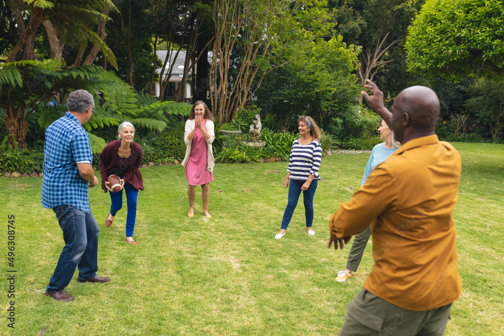 Fototapeta premium Multiracial active senior male and female friends playing rugby in backyard on weekend