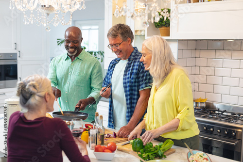Happy multiracial senior women and men preparing food together in kitchen at home