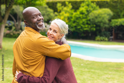 Fotografi Portrait of happy multiracial senior couple looking over shoulders in backyard