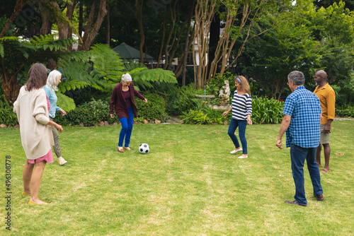 Multiracial active senior male and female friends playing soccer in backyard on weekend