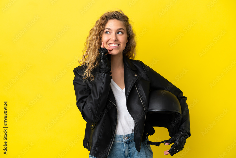 Young blonde woman with a motorcycle helmet isolated on yellow background thinking an idea while looking up Young blonde woman with a motorcycle helmet isolated on yellow background thinking an idea while looking up