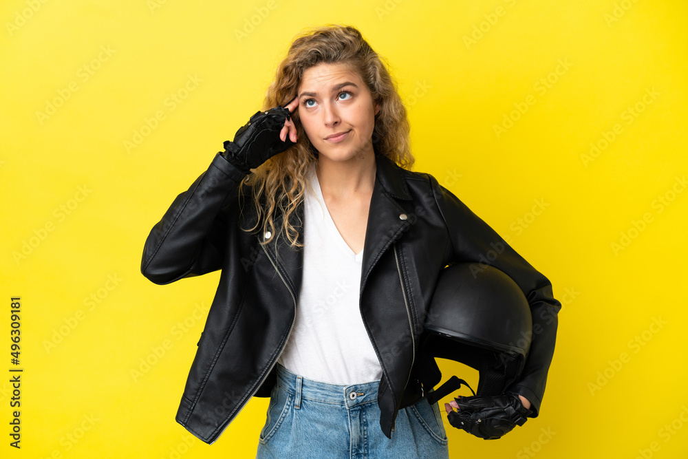 Young blonde woman with a motorcycle helmet isolated on yellow background having doubts and thinking Young blonde woman with a motorcycle helmet isolated on yellow background having doubts and thinking