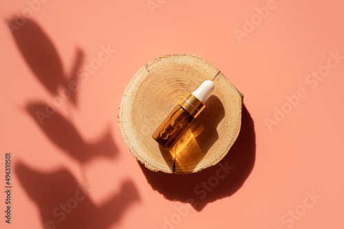 Amber glass dropper bottle on woodcut in the sunlight with eucalyptus flower shadows. Top view. Luxury and natural cosmetics presentation. Testers, beauty samples perfumery concept. Shades and lights © Lavsketch