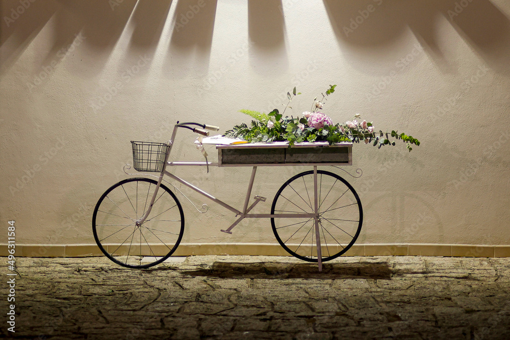 Bicicletta Vintage allestita con decorazioni floreali poggiata su un muto bianco 