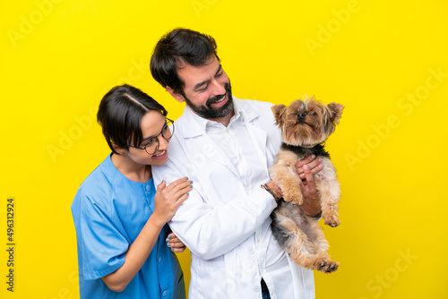 Young veterinarian couple with dog isolated on yellow background with happy expression