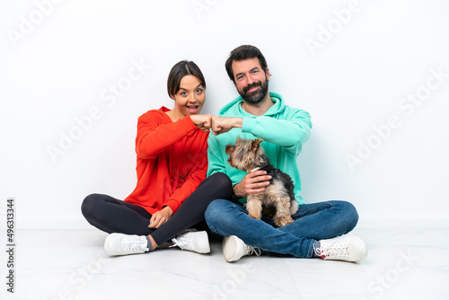 Young caucasian couple sitting on the floor with their pet isolated on white background bumping fists