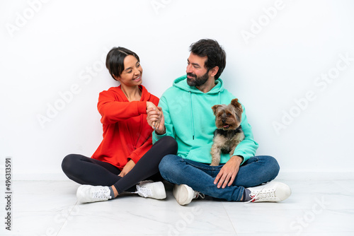 Young caucasian couple sitting on the floor with their pet isolated on white background handshaking after good deal