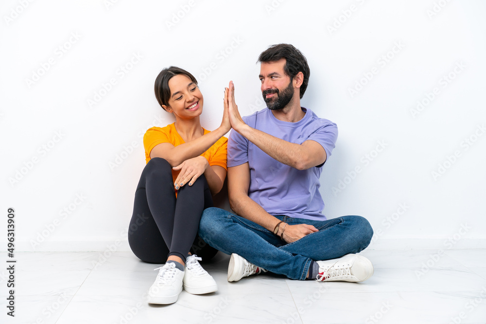 Young caucasian couple sitting on the floor isolated on white background bumping hands Young caucasian couple sitting on the floor isolated on white background bumping hands