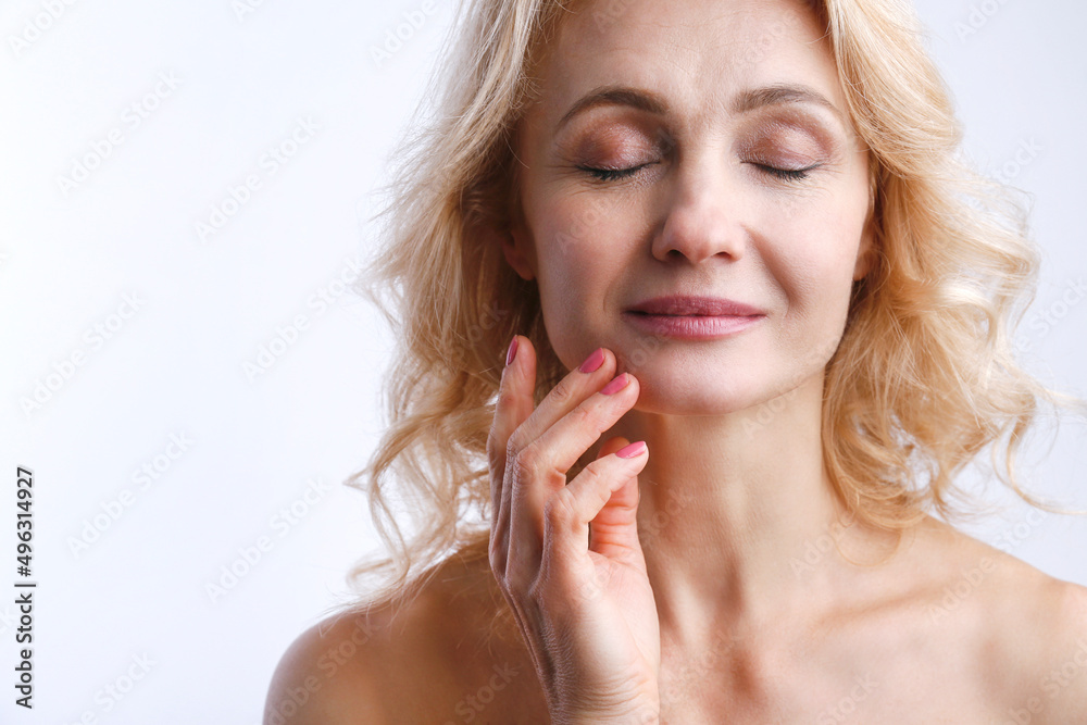 Studio portrait of sensual adult woman with clean smooth skin touching her face over isolated white background. Middle aged female with wavy blonde hair and naked shoulders. Close up, copy space. Studio portrait of sensual adult woman with clean smooth skin touching her face over isolated white background. Middle aged female with wavy blonde hair and naked shoulders. Close up, copy space.