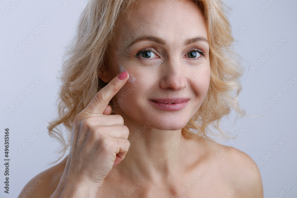Portrait of adult woman with perfectly clean face skin applying moisturizing cream. Mid aged female with wavy blonde hair smiling performing daily skincare routine. Close up, copy space background. Portrait of adult woman with perfectly clean face skin applying moisturizing cream. Mid aged female with wavy blonde hair smiling performing daily skincare routine. Close up, copy space background.