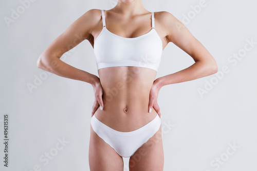 Close up shot of unrecognizable fit woman in lingerie isolated on white background. Torso of slim attractive female with flat belly in white underwear. Copy space for text.