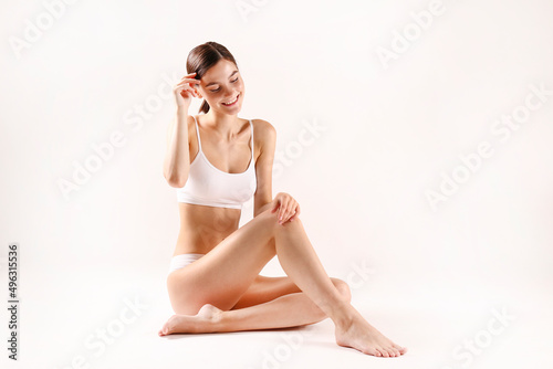 Studio shot of fit woman wearing seamless underwear in sitting on the floor isolated on white. Slim female with her hair tied in ponytail posing in white lingerie. Copy space, close up, background.