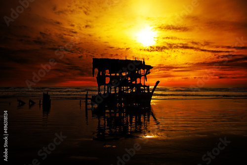 decaying metal and oil shipwreck on sand at sunset