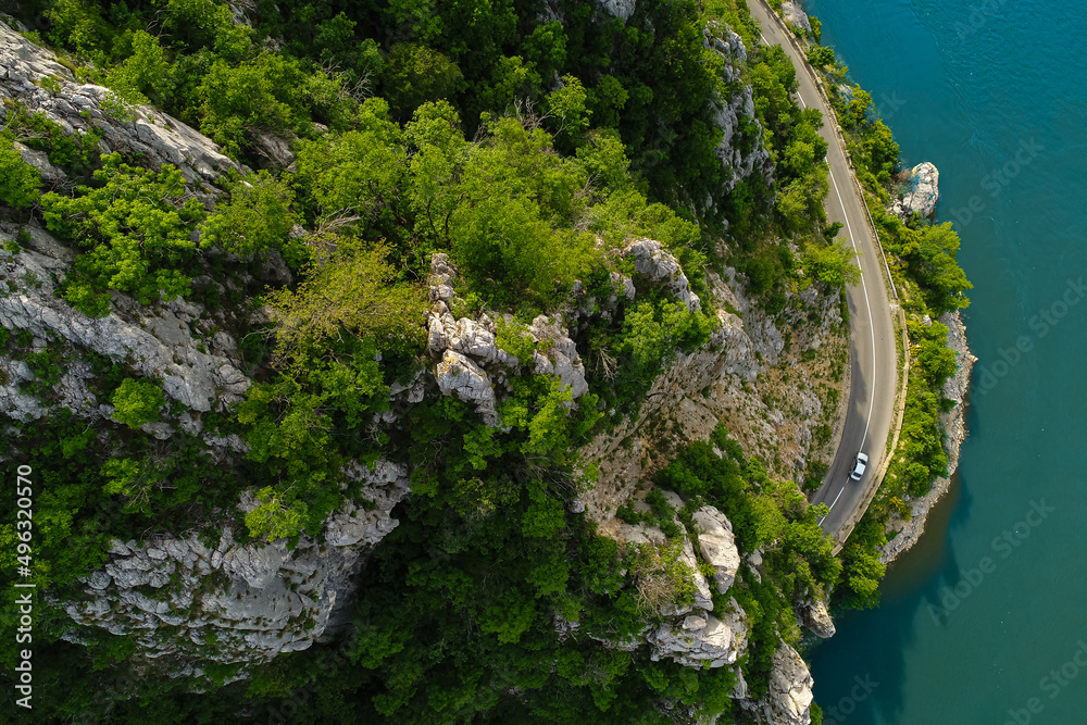 Aerial view of an amazing road on the coast line next to a river. Beautiful roads infrastructure around the world during a beautiful summer day.