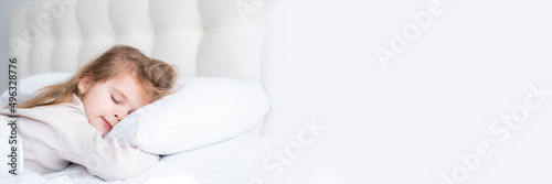 banner cute child girl with long hair in beige pyjamas sleeping on white bedding at home