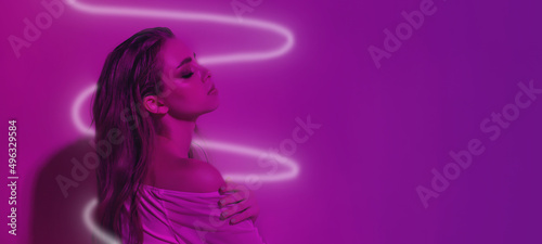Portrait of a female fashion model in neon pink light with a glowing spiral on a dark studio background. Beautiful woman with fashionable make-up and well-groomed skin. Bright style, future concept