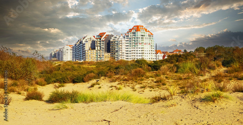 Konstfotografi View over sand dunes with grass on belgian modern coast town buildings against d