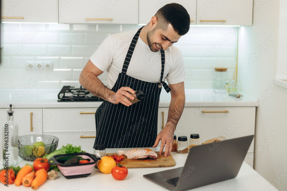 Smiling guy prepares vegetables in the kitchen. Dressed in a black apron Smiling guy prepares vegetables in the kitchen. Dressed in a black apron