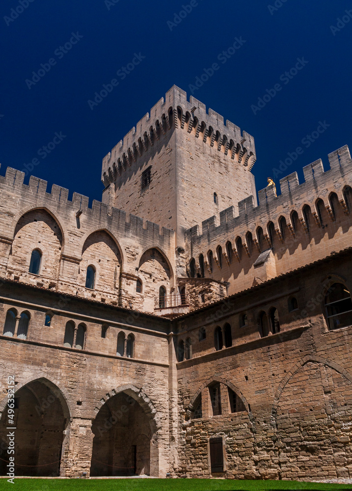 A historical wall tower on the corner of a castle standing under a blue sky in a sunny day in Avignon, Provence, France