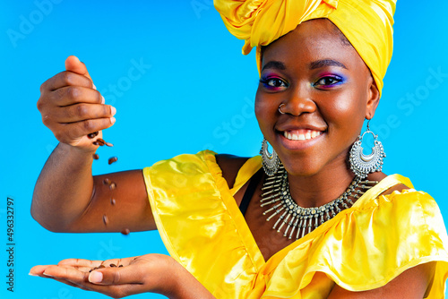 beautiful africa-american woman with yellow turban ower the head showing fresh coffee beand in studio blue baclground photo