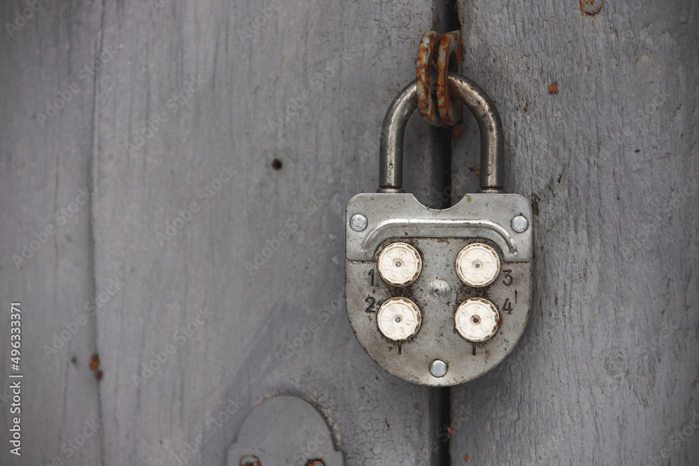 Old combination padlock hanging on grungy gray wooden door