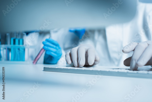 partial view of bioengineer in latex gloves typing on computer keyboard near colleague with test tube.