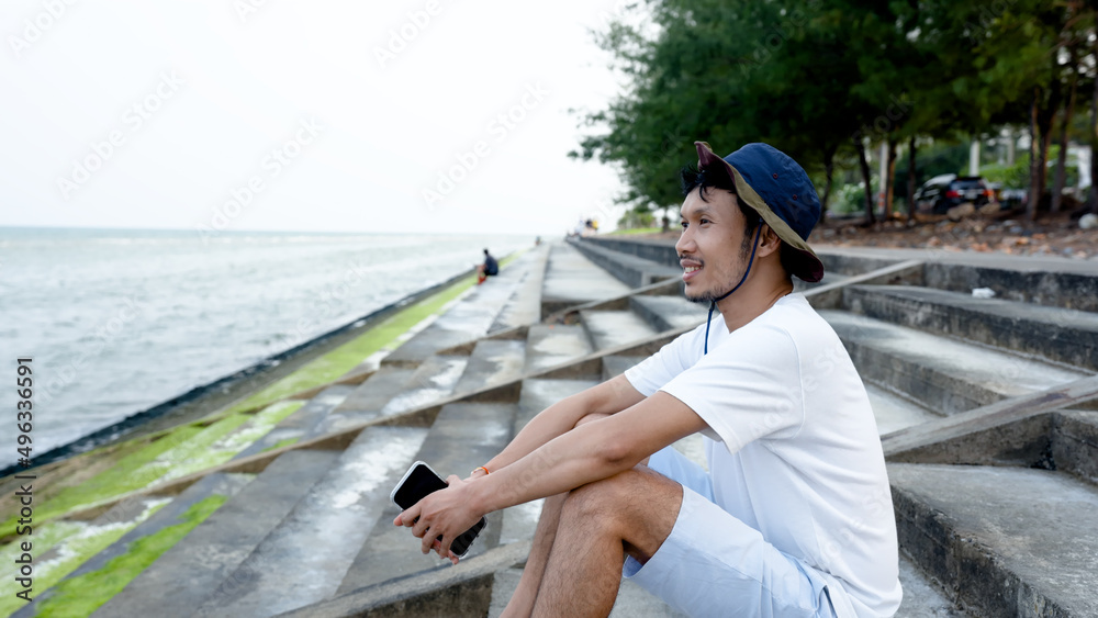 Good looking Asian guy, sitting alone on a beautiful beach, enjoying the cool breeze, popular tourist destination