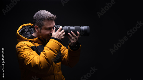 Photographer in a yellow coat taking a photo with a black background