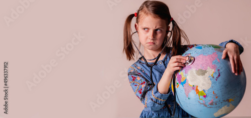 Beautiful young girl with stethoscope listening to the globe. Ecology, health, problem of war and peace concept. Copy space for design.