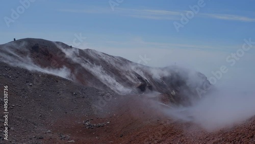 Silhouette of man hiking at coldera of Avachinsky stratovolcano, also known as Avacha Volcano. Backpacker tourist moves upon rocks behind steam from hot geysers. Kamchatka Peninsula, Russia.