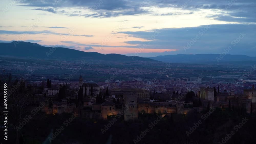 Alhambra Palace at dusk with faint city lights in backdrop Alhambra Palace at dusk with faint city lights in backdrop