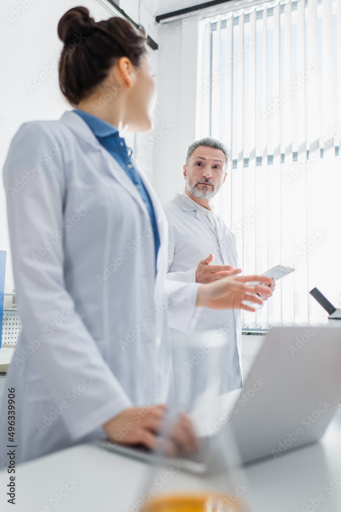 Obraz premium bioengineers with gadgets gesturing and talking in laboratory.