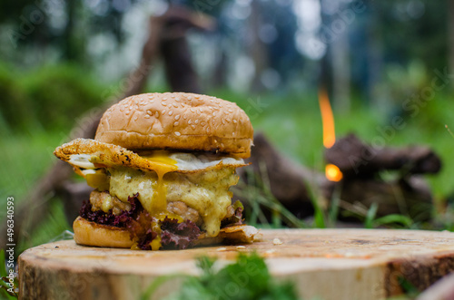 home made chicken burger with curry mayo sauce and lettuce, tomato, egg, green and yellow paprica as compliment. bushcraft cooking style with campfire.