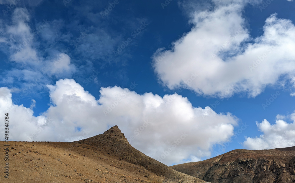 Dry inland mountains of the island of Fuerteventura in the Canary Islands under a blue cloudy sky.