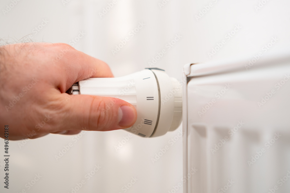 Man hand regulates temperature knob of the heating radiator to reduce heating costs. Man hand regulates temperature knob of the heating radiator to reduce heating costs.