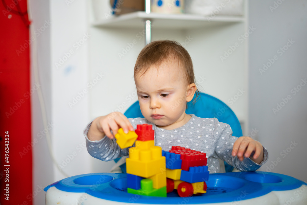 A child in a builder's helmet builds a house from colored blocks A child in a builder's helmet builds a house from colored blocks