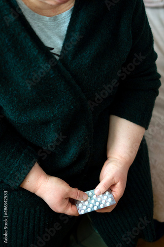 Sad old woman taking pills, health problems in old age, expensive medications. An elderly woman's hands unpacking several pills for taking medication.