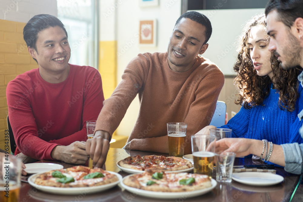 Smiling friends eating pizza at modern pizzeria restaurant - Friendship concept with multi ethnic people enjoying time together having fun at pizzeria with pizza and beer pints Smiling friends eating pizza at modern pizzeria restaurant - Friendship concept with multi ethnic people enjoying time together having fun at pizzeria with pizza and beer pints