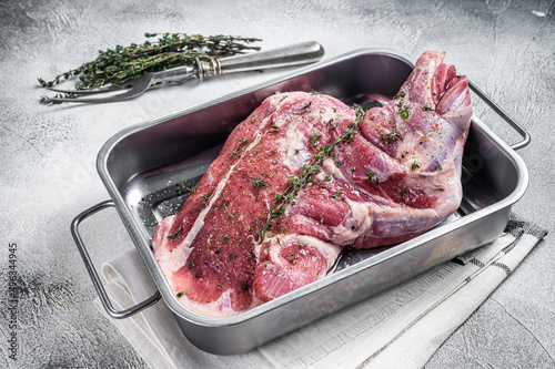 Marinated mutton lamb whole shoulder, raw meat in a steel tray with herbs and spices. White background. Top view. Copy space