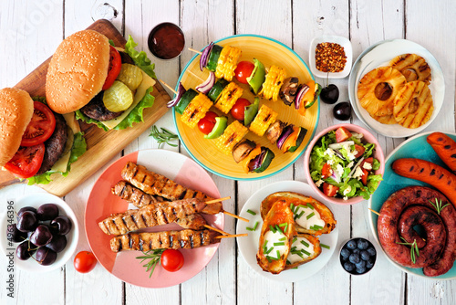 Summer BBQ or picnic food table scene. Selection of burgers, grilled meat, vegetables, fruits, salad and potatoes. Overhead view on a white wood background.
