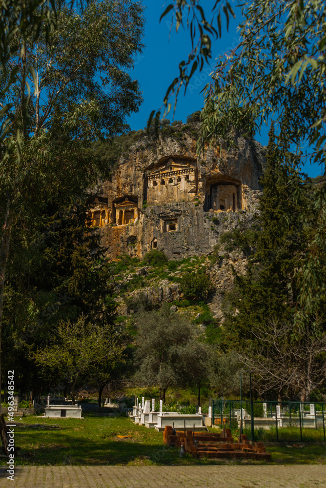 DALYAN, MUGLA, TURKEY: A modern Turkish cemetery and Lycian tombs carved into the rock in the ancient city of Kaunos. DALYAN, MUGLA, TURKEY: A modern Turkish cemetery and Lycian tombs carved into the rock in the ancient city of Kaunos.