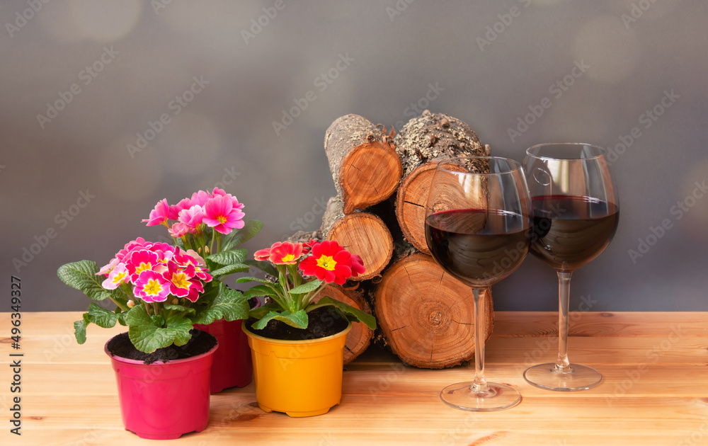 Primula flowers, glasses of red wine and pile of firewood on wooden table. Primula flowers, glasses of red wine and pile of firewood on wooden table.