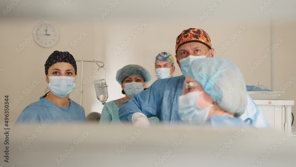 Team of surgeons performing operation in hospital. Surgeon male healthcare professional in a hospital operating theatre wearing a surgical cap and mask. Female doctor in medical uniform putting Team of surgeons performing operation in hospital. Surgeon male healthcare professional in a hospital operating theatre wearing a surgical cap and mask. Female doctor in medical uniform putting