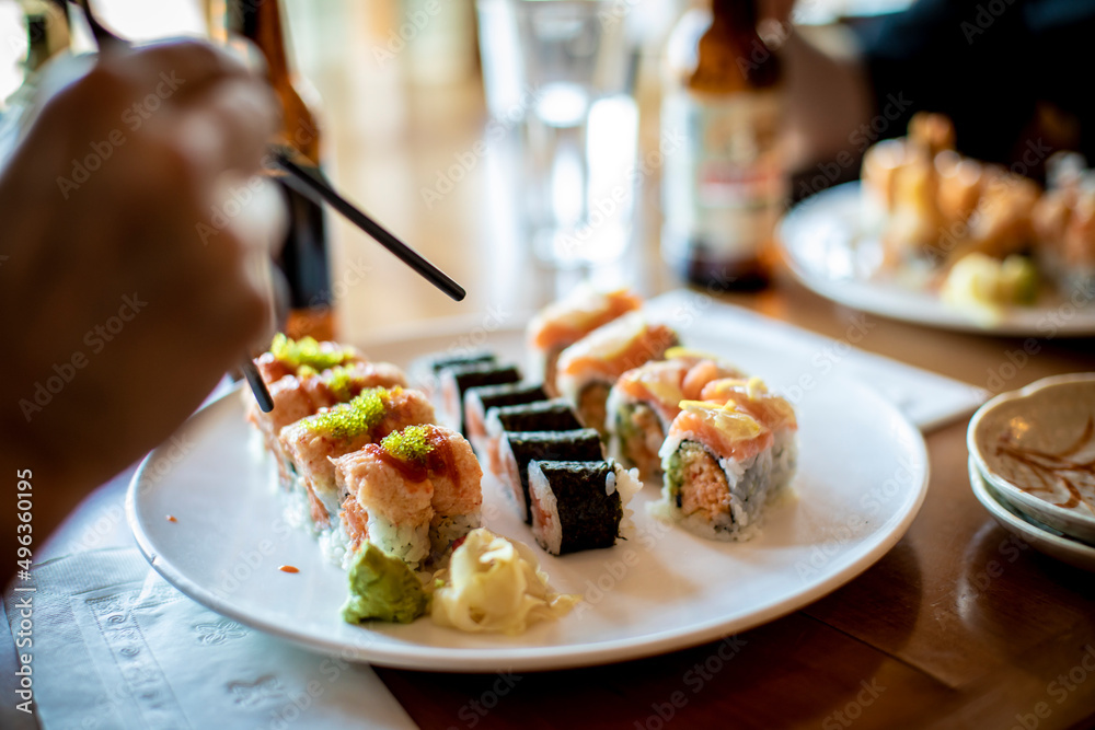 A hand holding chopsticks about to pick up a sushi roll. A hand holding chopsticks about to pick up a sushi roll.