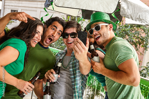 Group of friends hanging out on balcony taking a selfie and drinking beer celebrating St. Patrick's Dat. photo